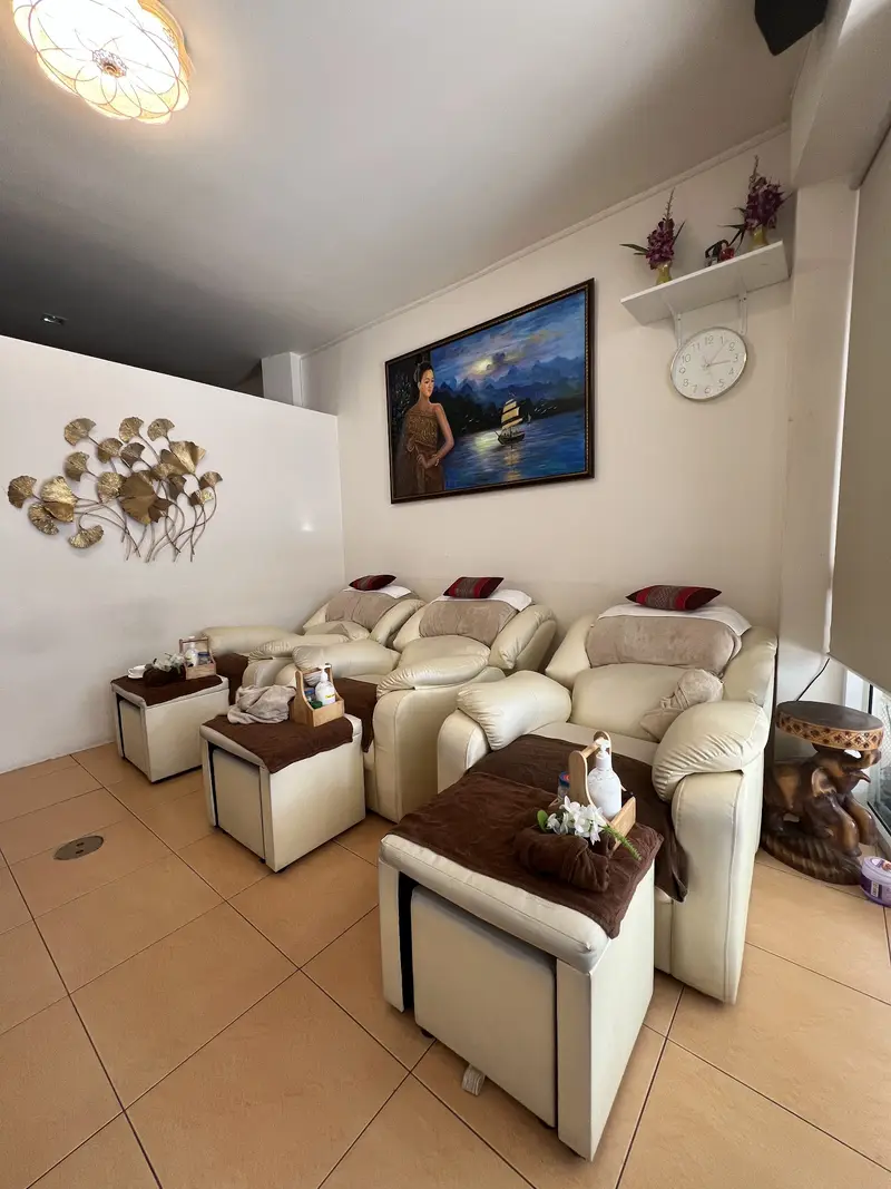 Three cream reclining armchairs for foot massage with towels and oils, under a painting of a Thai lady